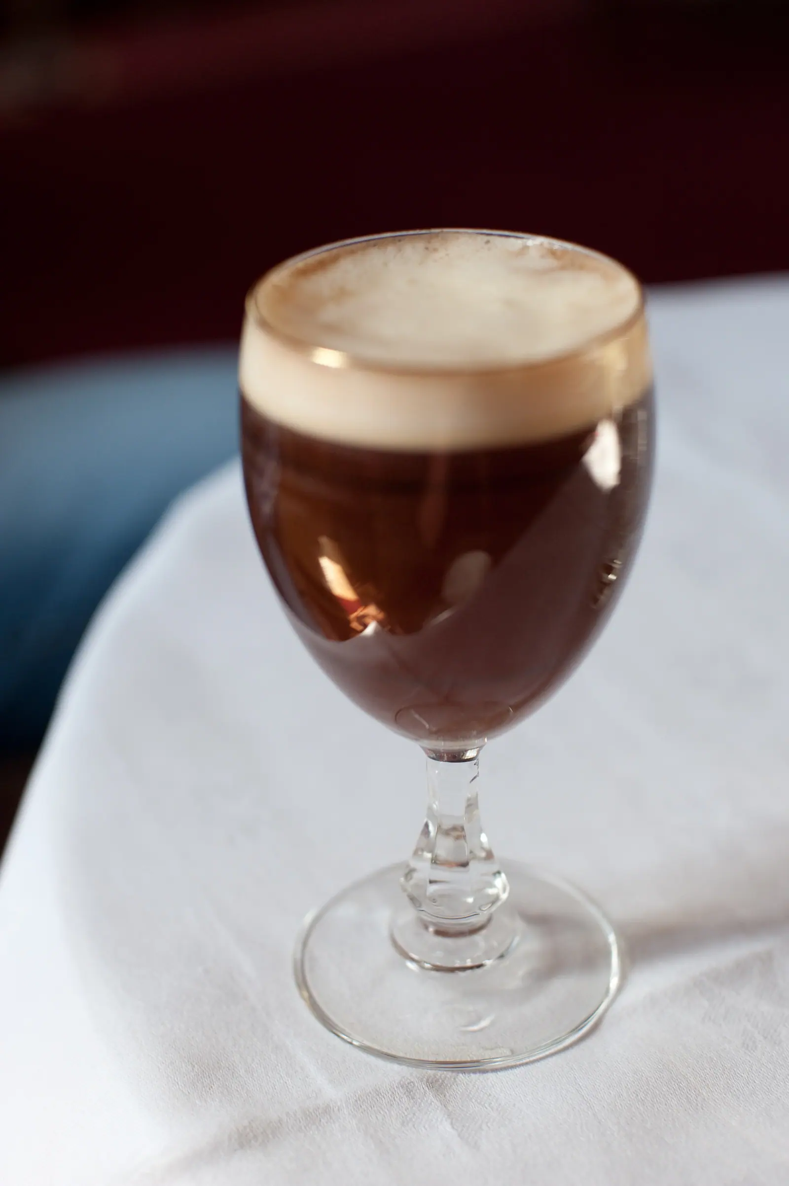 A dark coffee drink with foam in a stemmed glass on a white cloth