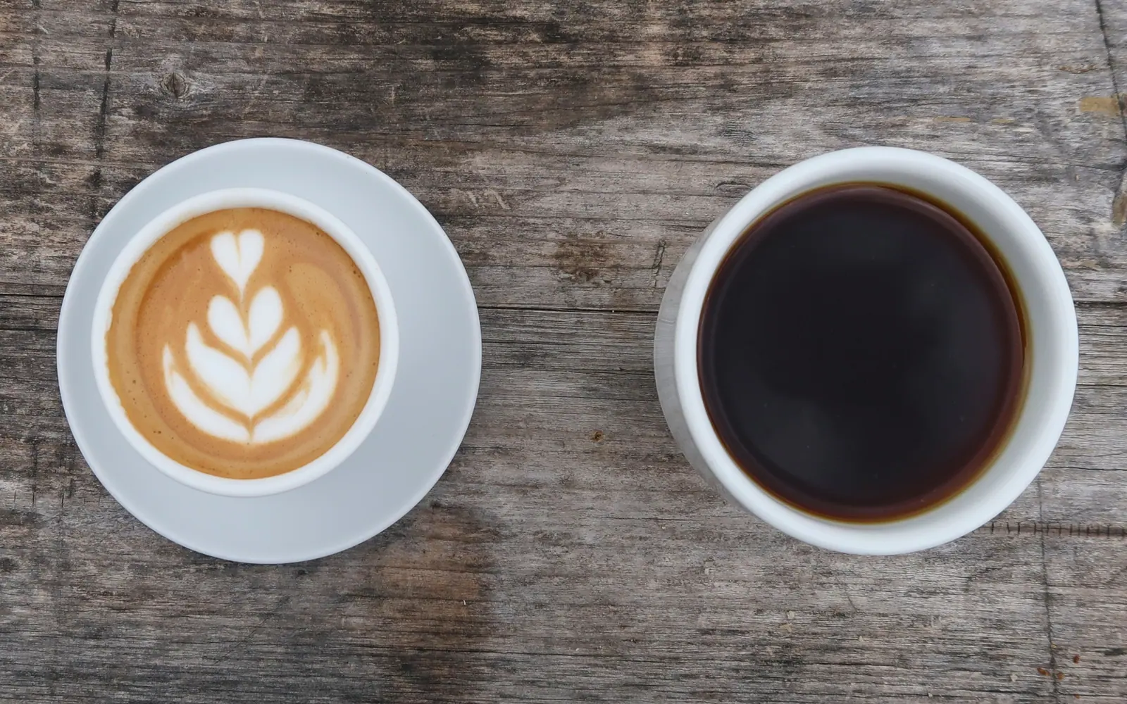 Overhead view of a latte and a black coffee on weathered wood