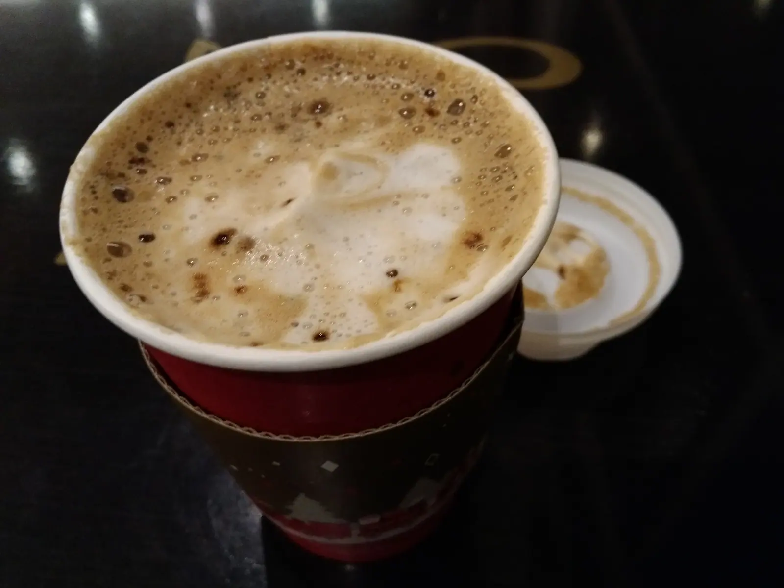 Foamy coffee in a red paper cup against a dark background
